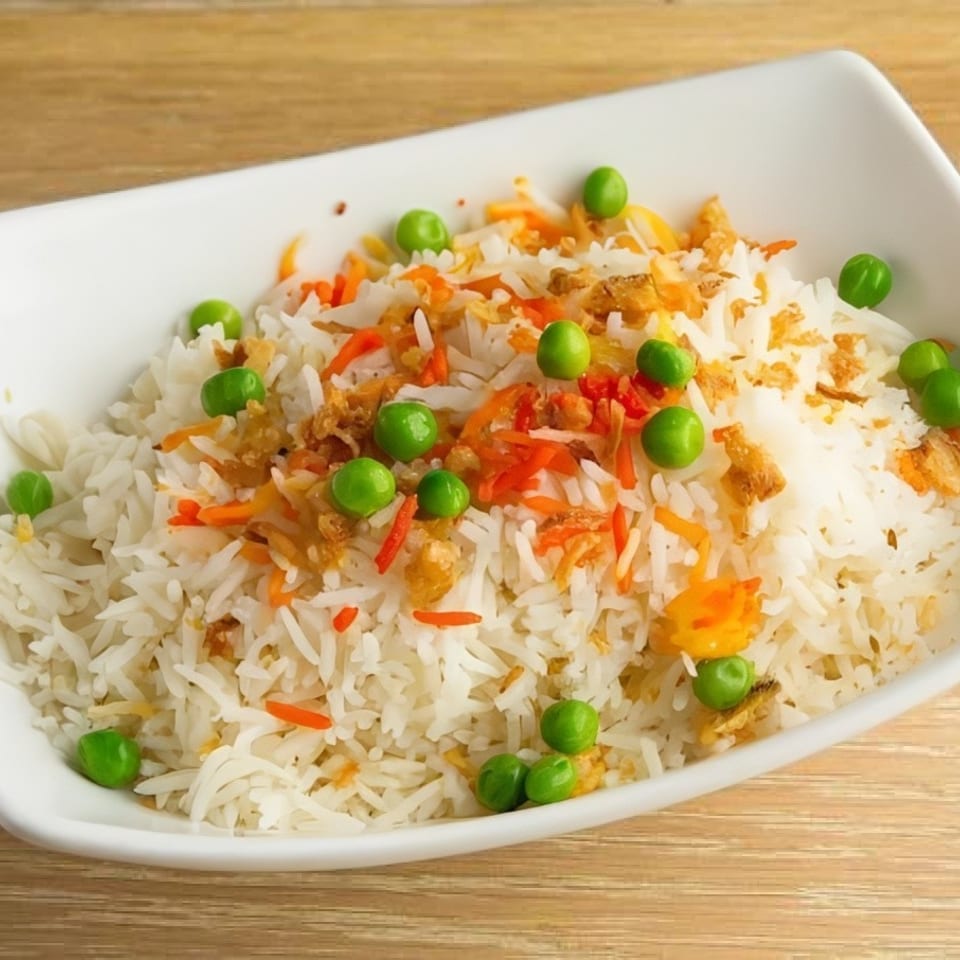 White rice with green peas, shredded carrots, and crispy fried onions in a white bowl.