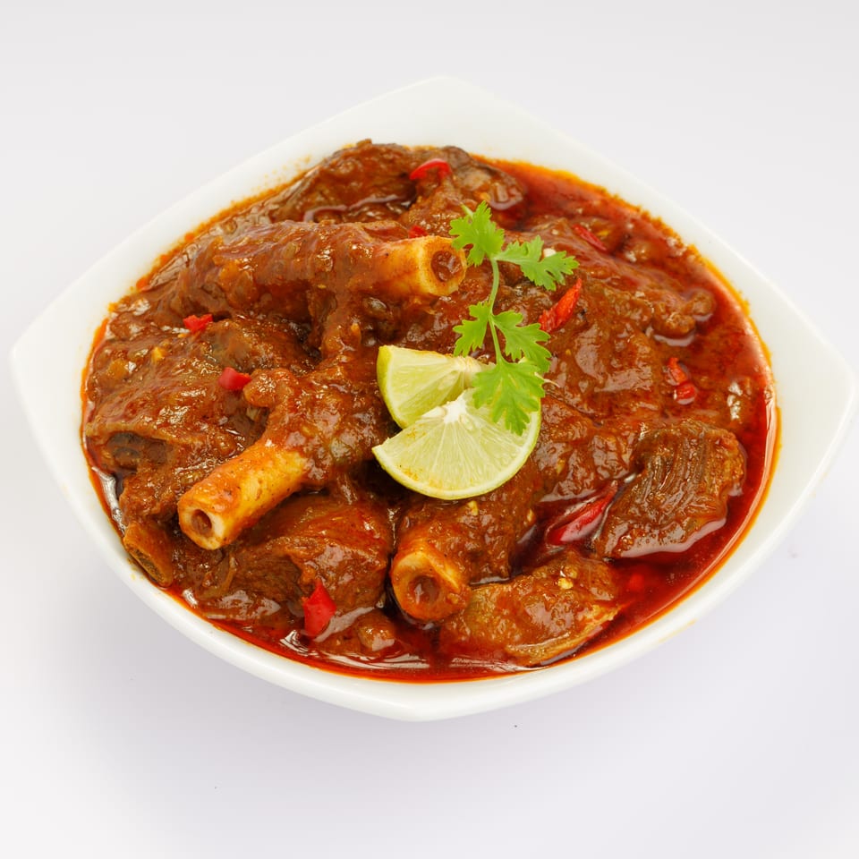 A white bowl filled with a rich, red curry featuring meat on the bone, garnished with lime and cilantro.